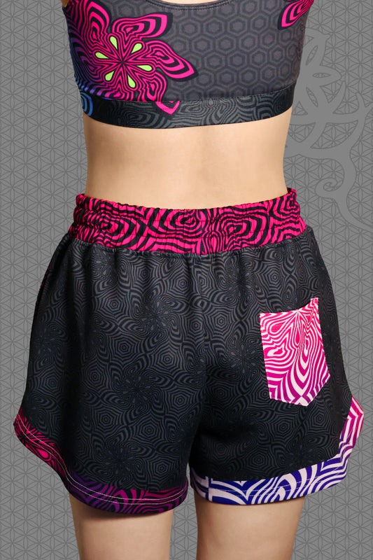 back view psychedelic loose-fit shorts with black geometric pattern body, magenta-to-purple optical pattern panels and waistband, gradient pink-purple-blue accents, drawstring waist, and contrasting patterned back pocket