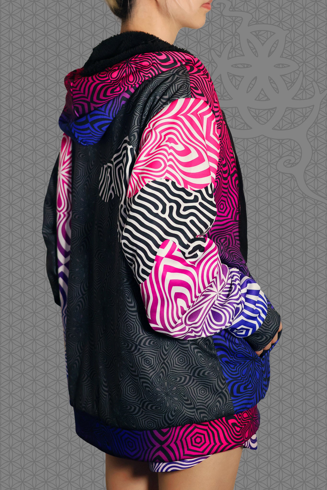 right view psychedelic rave zip hoodie with neon pink, purple, and blue geometric optical patterns and black panel design with black fleece interior lining