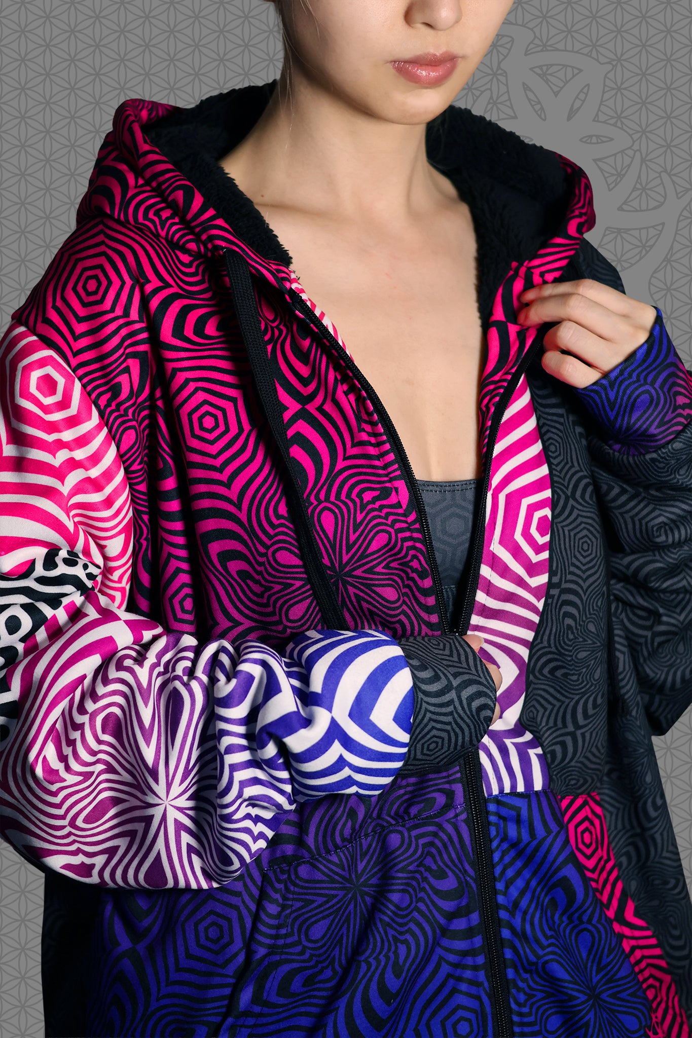 close-up view psychedelic rave zip hoodie with neon pink, purple, and blue geometric optical patterns and black panel design with black fleece interior lining