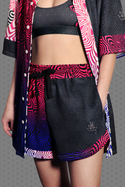 model view psychedelic loose-fit shorts with black geometric pattern body, magenta-to-purple optical pattern panels and waistband, gradient pink-purple-blue accents, drawstring waist, and contrasting patterned back pocket