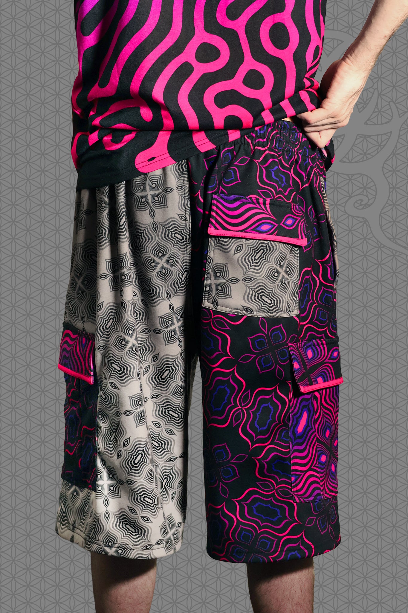 back view psychedelic cargo shorts with split design featuring grey geometric pattern on one side and vibrant pink-purple pattern on the other, with drawstring waist and side cargo pockets