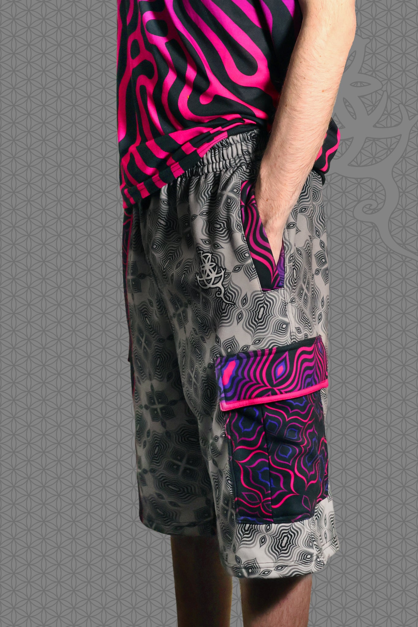 left view psychedelic cargo shorts with split design featuring grey geometric pattern on one side and vibrant pink-purple pattern on the other, with drawstring waist and side cargo pockets