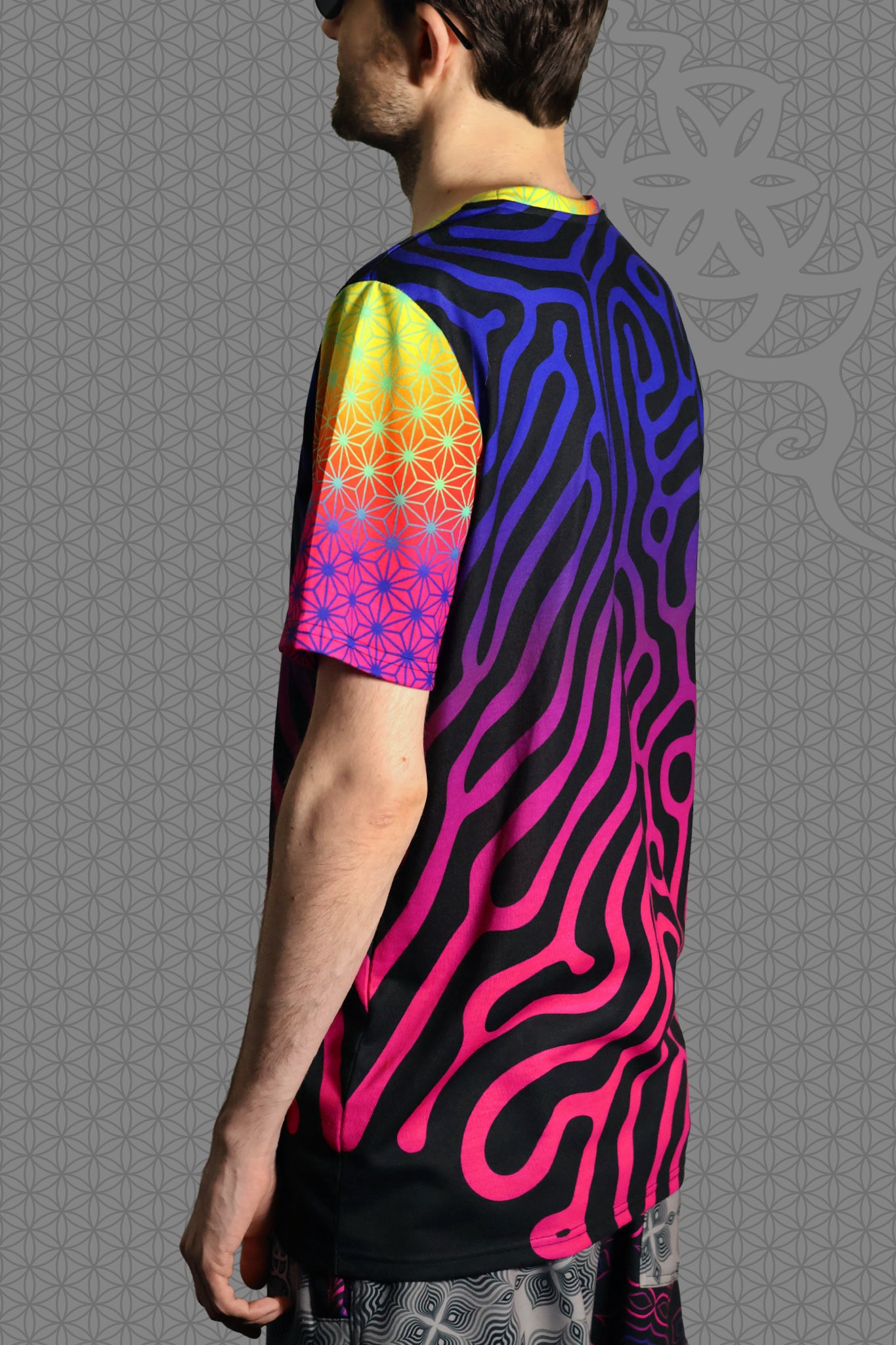 left view psychedelic short sleeve t-shirt with black base and flowing pink-to-purple gradient pattern, featuring contrasting rainbow geometric trim on the sleeve and collar
